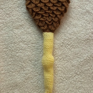May include: A crocheted brown and yellow dinosaur tail costume. The tail is made of brown yarn and has a scaly texture. The leg is made of yellow yarn and has a rounded shape.