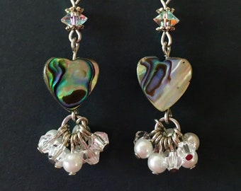 May include: A pair of dangle earrings featuring heart-shaped abalone shell charms, iridescent crystal bicone beads, and clusters of small white pearls and clear faceted crystal beads suspended from silver-toned metal hooks and hardware.