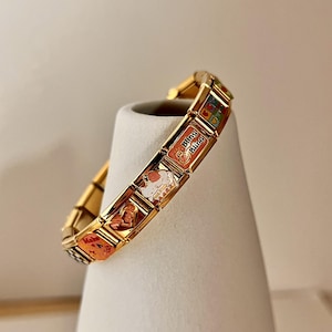 May include: Gold charm bracelet with various charms, including a heart charm with "Make a Wish" text, a charm with a white cat, and a charm with "Bling Bling" text.