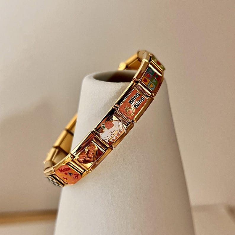 May include: Gold charm bracelet with various charms, including a heart charm with "Make a Wish" text, a charm with a white cat, and a charm with "Bling Bling" text.