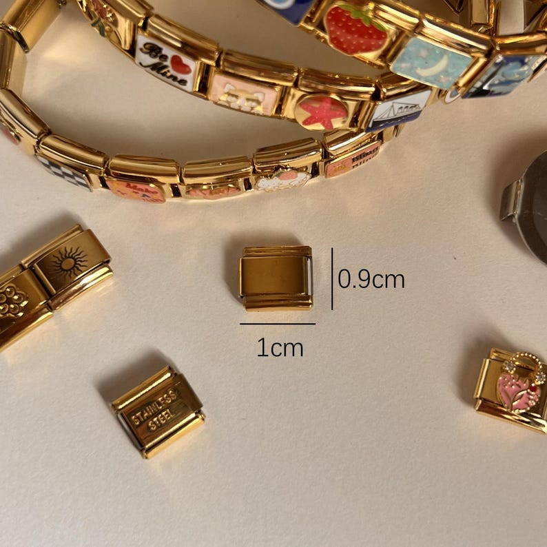 May include: Gold-toned metal charm bracelet with various charms, including a strawberry, a star, and a sailboat. The bracelet is 0.9 cm wide and 1 cm long.