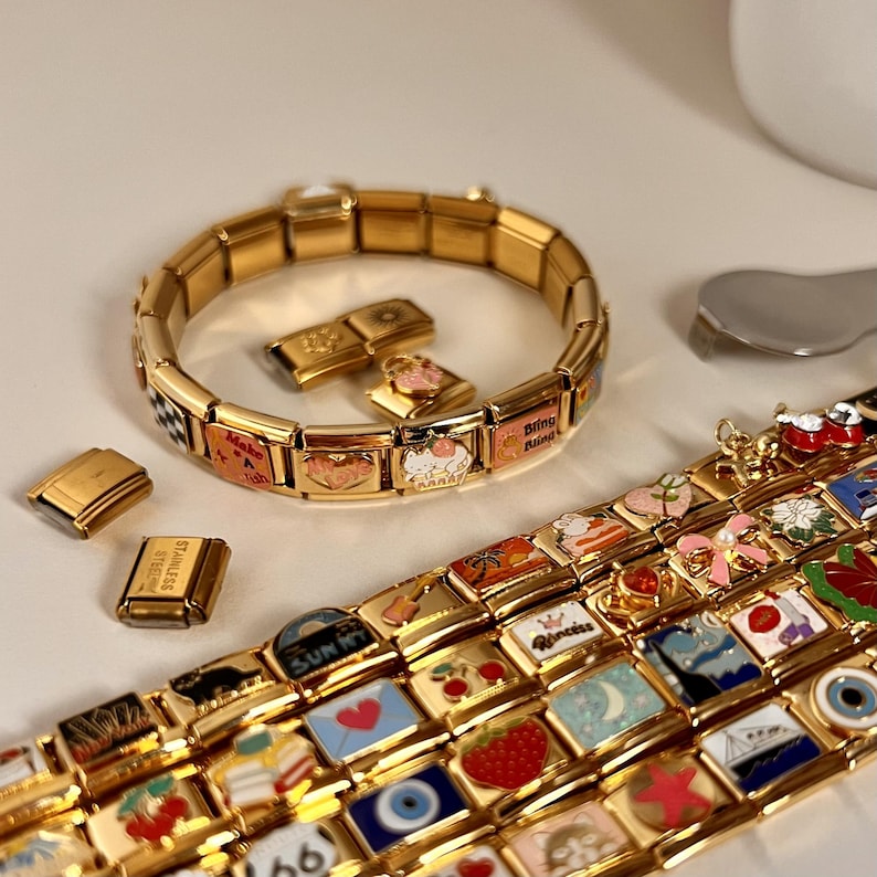 May include: A gold charm bracelet with various charms, including hearts, a cloud, a cat, a strawberry, a sailboat, and a sun. The charms are attached to a gold chain bracelet.