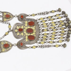 May include: A silver and gold necklace with red carnelian stones and a pendant with a floral design. The necklace has a chain with bells.