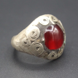 May include: A silver ring with a red gemstone set in a decorative swirl design.