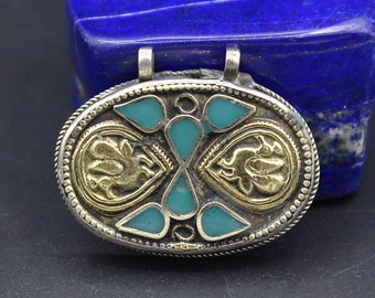 May include: Oval pendant with silver-tone metal, gold-tone accents, and turquoise-colored inlays. The pendant features two stylized gold figures and teardrop-shaped turquoise stones. The pendant has two small loops at the top for hanging.