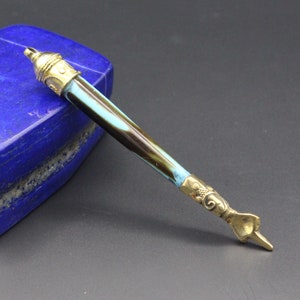 Może przedstawiać: Dekoracyjne pióro z niebiesko-brązowym wzorzystym uchwytem i złotymi akcentami. Pióro ma spiczasty grot i ozdobny wzór na końcu uchwytu.