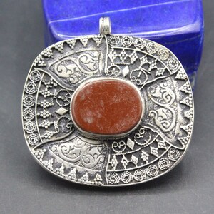 May include: A silver pendant with intricate filigree designs and a red stone in the center.