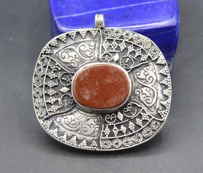 May include: A silver pendant with intricate filigree designs and a red stone in the center.