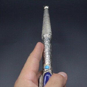 May include: A silver and blue decorative stick with intricate designs and a turquoise stone.