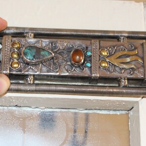 Puede incluir: Cerrojo de puerta plateado adornado con piedras turquesas y &aacute;mbar, y detalles dorados. El cerrojo tiene un dise&ntilde;o decorativo. El cerrojo de la puerta es un elemento decorativo.