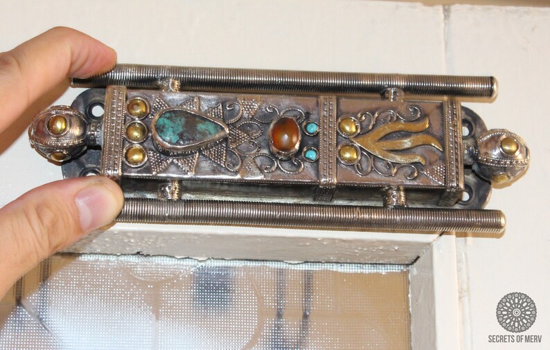 Puede incluir: Cerrojo de puerta plateado adornado con piedras turquesas y &aacute;mbar, y detalles dorados. El cerrojo tiene un dise&ntilde;o decorativo. El cerrojo de la puerta es un elemento decorativo.