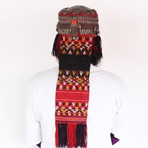 Peut inclure: Un chapeau traditionnel brodé de rouge et de noir avec des embellissements argentés et des glands. Le chapeau est porté par une personne aux cheveux longs et foncés.
