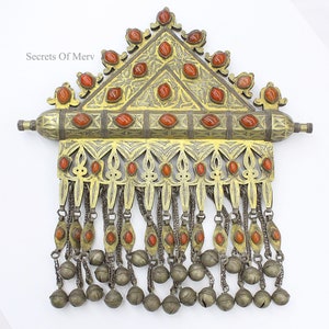 May include: A gold and silver ornate pendant with a triangular top and a long fringe of chains and bells. The pendant is decorated with red carnelian stones.
