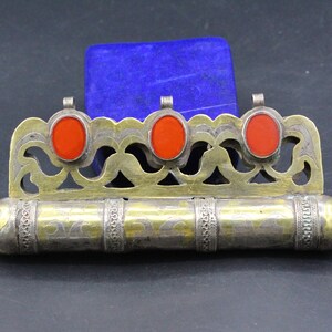 May include: A silver and gold ornate box with three red carnelian stones. The box is decorated with intricate floral designs and has a cylindrical shape.