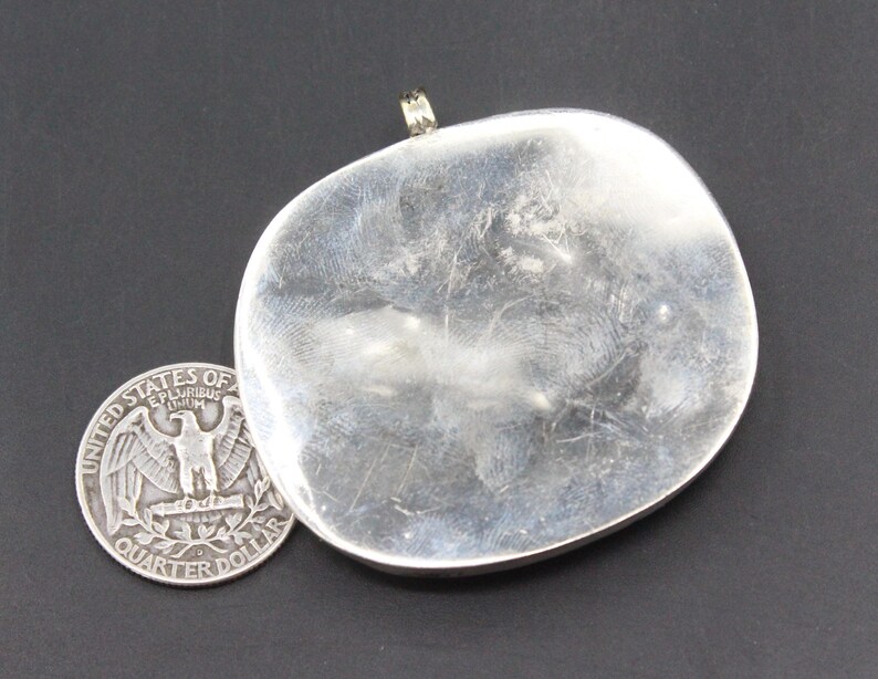 May include: A silver pendant with a smooth, rounded surface. The pendant has a loop at the top for attaching a chain.