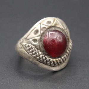 May include: A silver ring with a red gemstone set in a geometric design.