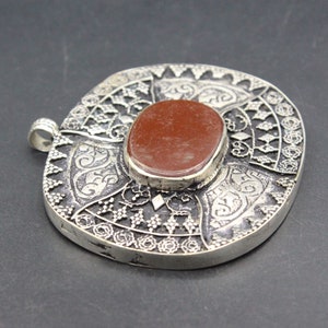 May include: A silver pendant with intricate filigree designs and a red gemstone in the center.