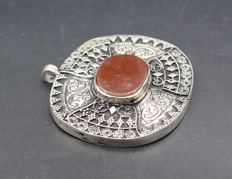 May include: A silver pendant with intricate filigree designs and a red gemstone in the center.