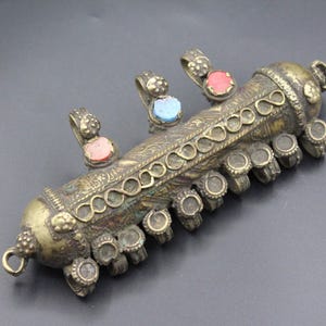 May include: Antique silver-toned pendant with intricate engraved patterns. The pendant features three small gemstone accents in pink and turquoise, and multiple circular embellishments. A unique piece of jewelry.