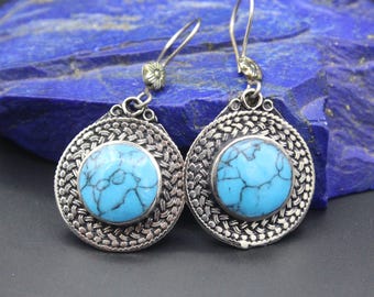 May include: A pair of silver earrings with turquoise stones set in a woven design. The earrings have a circular shape and are suspended from a silver hook.