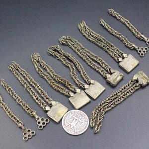 Pode incluir: Uma cole&ccedil;&atilde;o de pe&ccedil;as de corrente de metal prateado antigas, algumas com elementos decorativos quadrados ou circulares. As correntes est&atilde;o dispostas sobre uma superf&iacute;cie cinza escuro, com uma moeda vis&iacute;vel para escala.