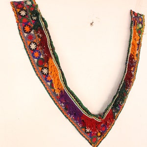 Puede incluir: Un ribete bordado de colores con borlas, que presenta un diseño en forma de V. El ribete está hecho de varios colores, incluyendo rojo, verde, azul y naranja.