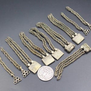 Pode incluir: Uma variedade de pulseiras antigas de corrente prateada com fechos quadrados e extremidades decorativas. As pulseiras est&atilde;o dispostas sobre uma superf&iacute;cie escura, com uma moeda de um quarto de d&oacute;lar americano para escala.