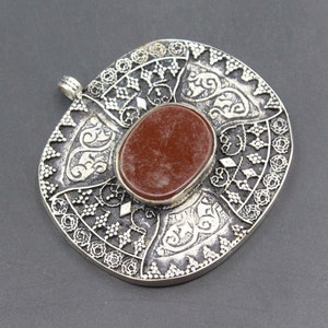 May include: A silver pendant with an intricate design and a red stone in the center.