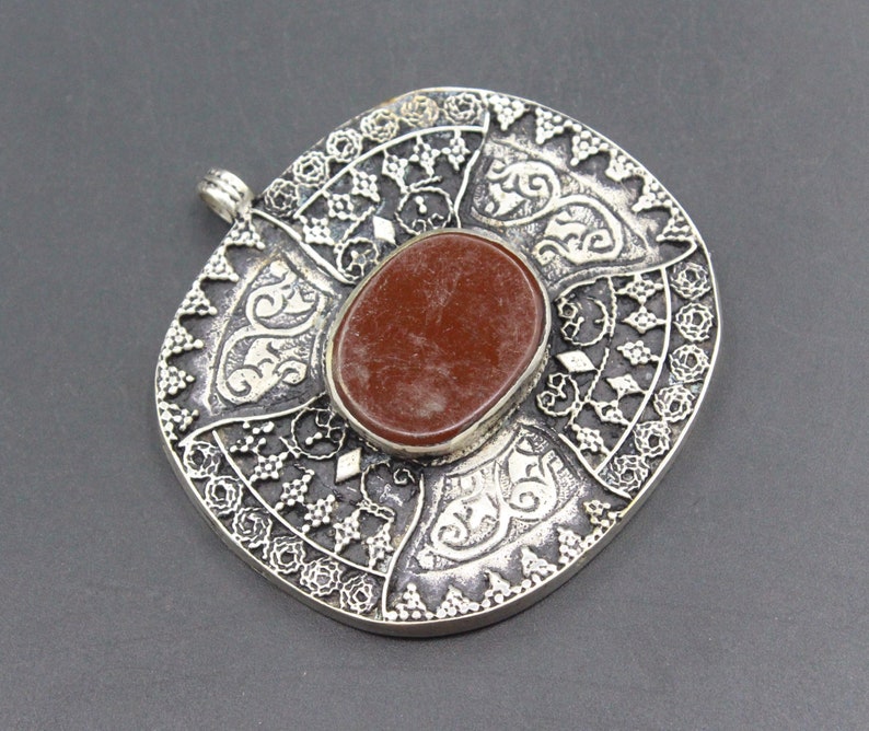 May include: A silver pendant with an intricate design and a red stone in the center.