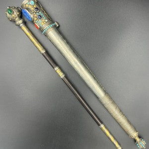 May include: A silver and gold ceremonial staff with a decorative handle and a long, slender shaft. The handle is adorned with colourful gemstones and intricate patterns.