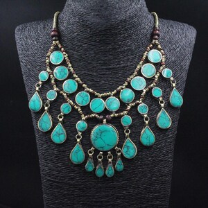 May include: A turquoise and gold necklace with a layered design and teardrop-shaped pendants.