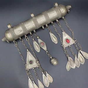 May include: A silver and red metal decorative piece with a cylindrical shape and multiple dangling chains. The chains have small, leaf-shaped pendants and red gemstone accents.
