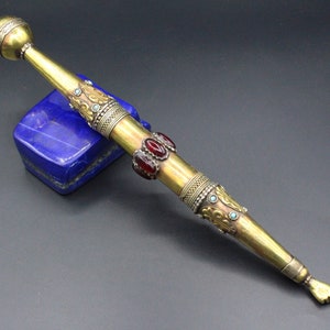 Może przedstawiać: Złota i srebrna ozdobna laska ceremonialna z zaokrąglonym wierzchołkiem i dłonią wskazującą do przodu na końcu. Laska jest ozdobiona czerwonymi i niebieskimi kamieniami szlachetnymi.