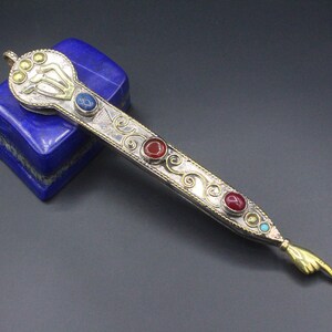 May include: A silver and gold decorative pointer with red and blue gemstones. The pointer has a hand-shaped tip and intricate scrollwork.