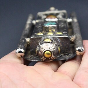 Puede incluir: Un colgante de metal plateado con un cuerpo rectangular y dos barras largas y paralelas. El colgante est&aacute; adornado con piedras de color turquesa y &aacute;mbar, y detalles dorados. El dise&ntilde;o tiene una est&eacute;tica vintage o antigua.