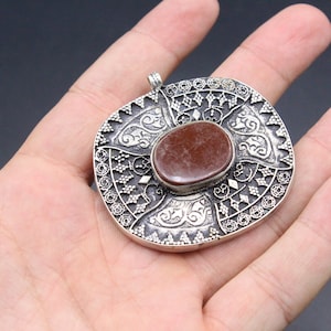 May include: A silver pendant with an intricate design and a red stone in the center.