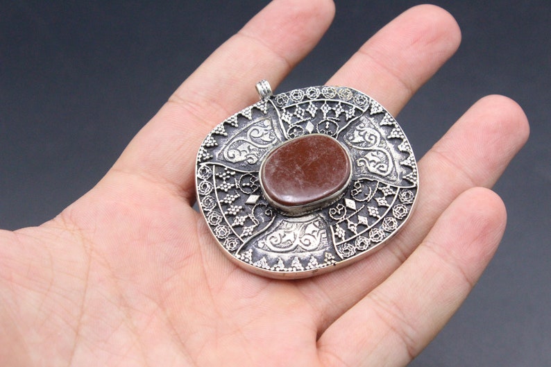May include: A silver pendant with an intricate design and a red stone in the center.
