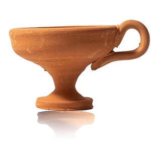 Könnte beinhalten: Eine Terrakotta-Tasse mit Henkel, mit einer breiten Schale und einem Sockel. Die Tasse hat ein rustikales, handgemachtes Aussehen mit einem natürlichen, erdigen Ton. Der Griff ist gebogen und an der Seite der Tasse befestigt.