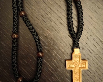 May include: A black prayer rope with wooden beads and a wooden cross pendant. The cross has the inscription "INRI" and a depiction of Jesus Christ.