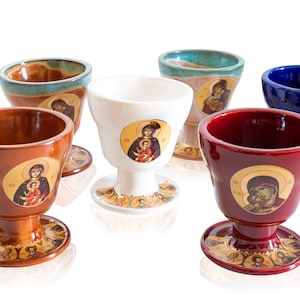 Pode incluir: Um conjunto de seis cálices de cerâmica em várias cores, incluindo castanho, branco, vermelho e azul. Cada cálice apresenta um ícone religioso e assenta numa base decorativa. Os cálices têm uma forma única, adequados para cerimónias religiosas.