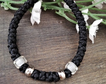 May include: A black braided bracelet with silver beads and clear glass beads.