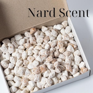 May include: An open cardboard box filled with small, light-colored stones, labeled "Nard Scent." A separate box with Greek text and a drawing of a building is next to it. The box is labeled 100 gr.