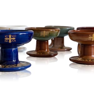 May include: Several ceramic chalices in shades of blue, brown, green, and white. Each chalice has a wide bowl, a pedestal base, and decorative details. The blue chalice has the text "IC XC NIKA".