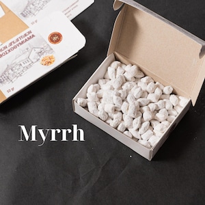 May include: A white box with the lid open, revealing a pile of white, powdery incense. The box is labelled "Аромат Афродиты" and "МОЖЖЕВЕЛЬНИК" in Cyrillic script. The word "Myrrh" is written in white text on a black background below the box.