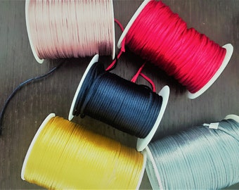 Puede incluir: Seis carretes de cordón en diferentes colores: rosa, rojo, negro, amarillo, gris y blanco. Los carretes están sobre una superficie de madera.