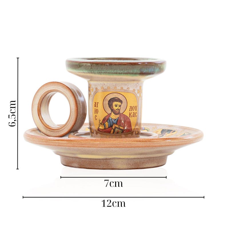 May include: A ceramic candle holder with a circular handle and a saucer base, featuring a religious icon print of Saint Luke. The item measures 6.5 cm in height, with a 7 cm inner base diameter and a 12 cm total width, finished in earthy brown tones.