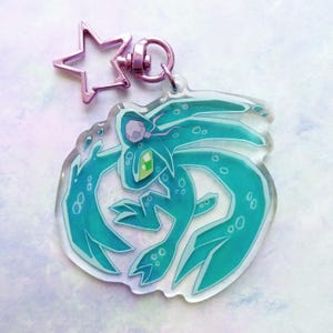 May include: A clear acrylic keychain featuring a teal cartoon creature with a green eye and a purple head. The keychain has a pink star-shaped charm and a pink clasp.