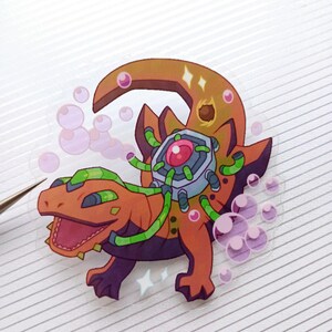 May include: A sticker featuring a cartoon lizard with orange, green, and purple accents. The lizard has a mechanical component on its back and is surrounded by pink bubbles. The sticker is on a white, lined surface.