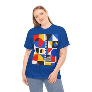 May include: A royal blue t-shirt with a vibrant geometric pattern. The design incorporates red, yellow, blue, and black shapes, such as circles, squares, and triangles. The person is wearing blue jeans.