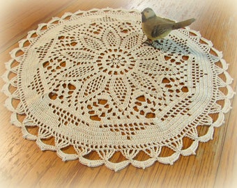 May include: A delicate, cream-colored crocheted doily with a circular design and a scalloped edge. A small, brown bird figurine sits on top of the doily.